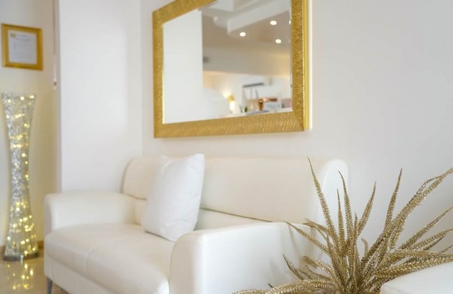 Divano bianco con specchio dorato e pianta decorativa.