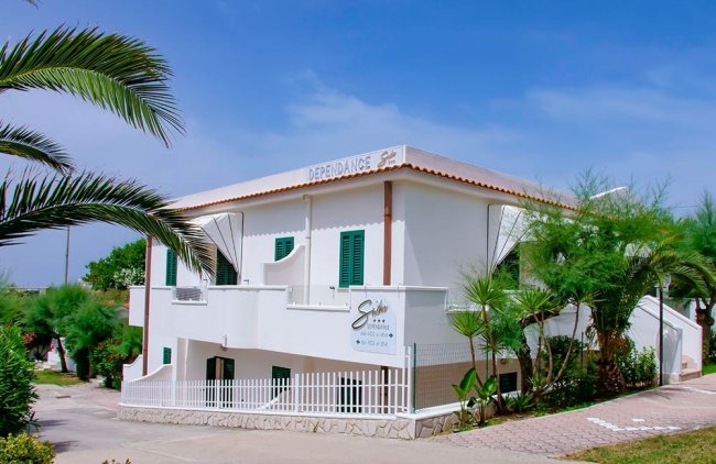 Edificio bianco con palme e arbusti.
