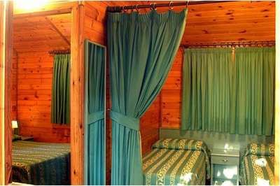 Due letti singoli in una stanza di legno con tende verdi che dividono lo spazio.