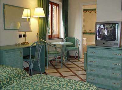 Una camera d'albergo con letti gemelli, TV, lampada e scrivania verde.