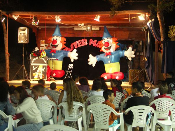 Uno spettacolo con clown gonfiabili giganti e pubblico seduto su sedie di plastica bianca.