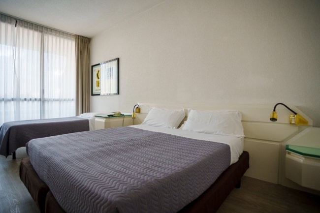 Camera d'hotel con due letti coperti da coperte viola.
