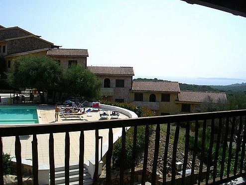Vista su piscina e case con tetti rossi immersi nel paesaggio collinare.