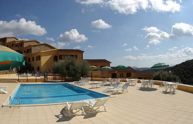 Piscina all'aperto circondata da sedie a sdraio e ombrelloni sotto un cielo soleggiato.