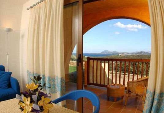 Sala con tavolo e fiori, porta su balcone con vista mare, divano blu visibile.