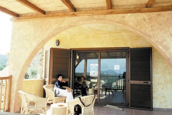 Una donna seduta su una sedia di vimini sotto una veranda coperta.