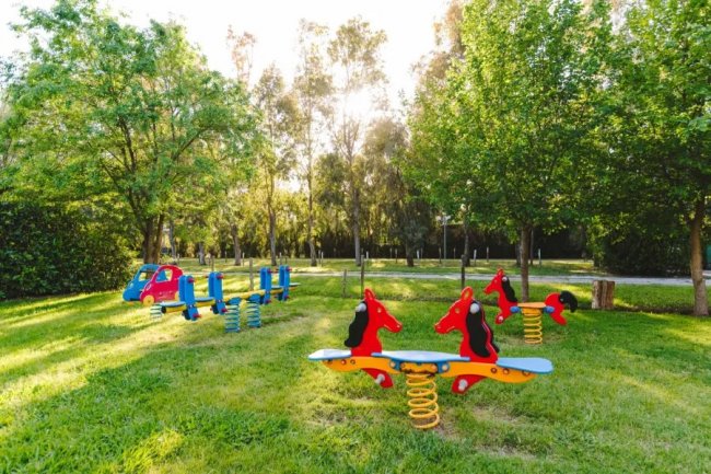 Area giochi con dondoli a molla a forma di cavallo e auto rossa su prato.