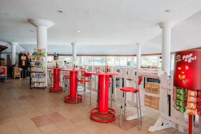 Un'area ristoro con tavolini rossi, sedie e distributori automatici.