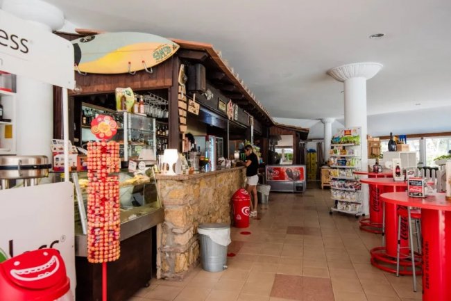 Un bar con bancone in pietra, espositore di bibite e una tavola da surf appesa.