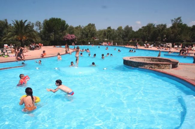 Bambini giocano in una piscina all'aperto, circondata da alberi.