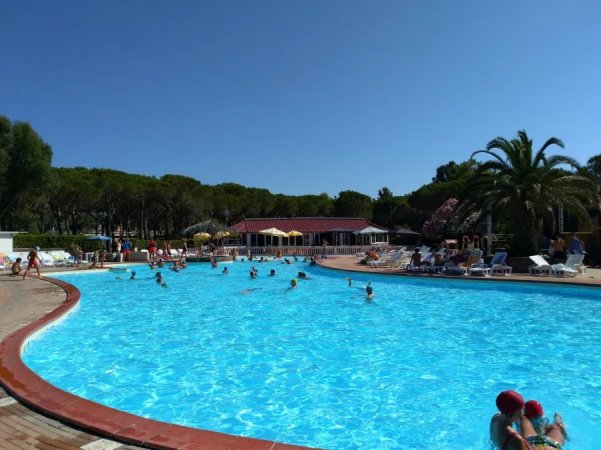 Piscina all'aperto con persone che nuotano, circondata da lettini e ombrelloni.