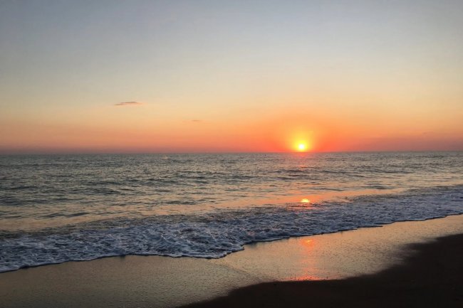 Tramonto sul mare, con il sole che cala all'orizzonte e onde che lambiscono la spiaggia.