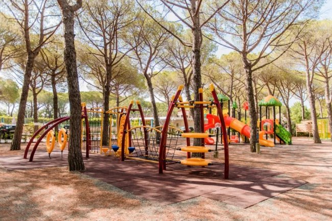 Parco giochi tra gli alberi, con strutture colorate per arrampicarsi e scivoli.