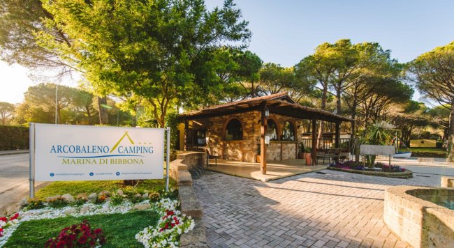 Ingresso del campeggio Arcobaleno con segnaletica e giardino fiorito.