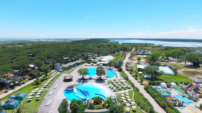 Villaggio turistico con piscine e bungalow, circondato da natura.