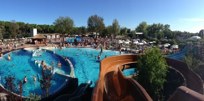 Piscina affollata con scivoli e ombrelloni.