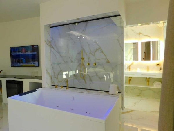 Bagno con doccia in marmo e rifiniture dorate.