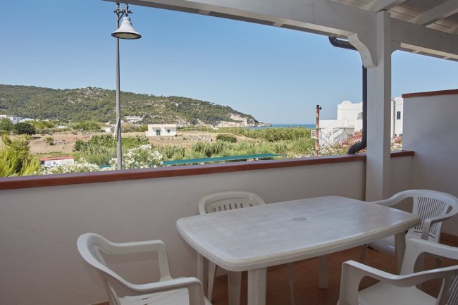 Terrazza coperta con tavolo bianco e sedie, vista collinare.