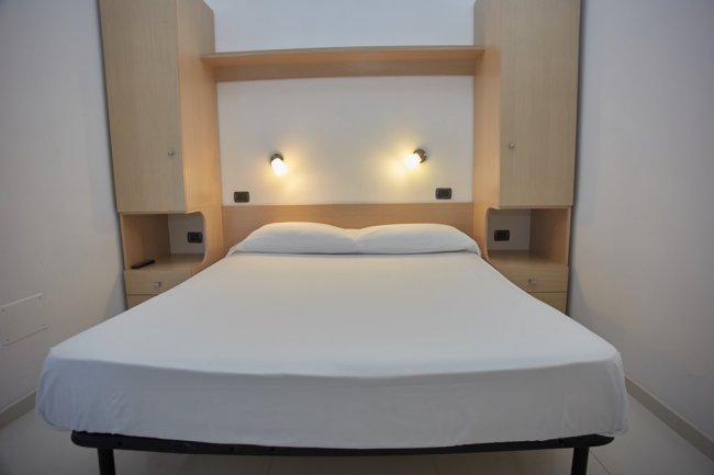 Letto matrimoniale con luci sopra, arredamento chiaro.