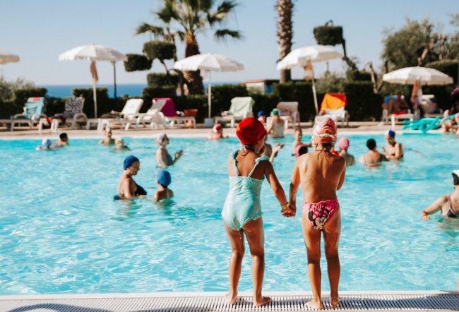 Due bambini con cuffie in piedi a bordo piscina.