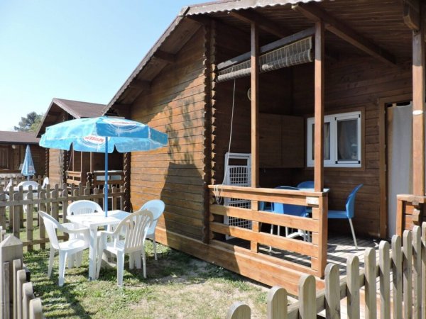 Una casetta di legno con veranda, tavolo e sedie bianche all'aperto sotto un grande ombrellone blu.