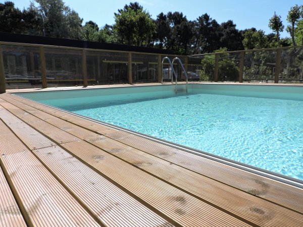 Piscina con acqua azzurra e bordo in legno, circondata da alberi.