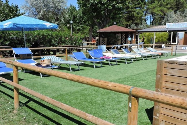 Lettini blu su erba sintetica con ombrelloni e recinzione in legno.