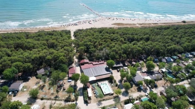 Vista aerea di una località costiera con case e piscina, circondata da foresta e spiaggia.