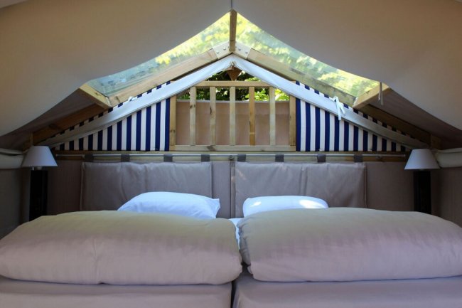 Interno di una tenda con letto matrimoniale sotto soffitto spiovente.