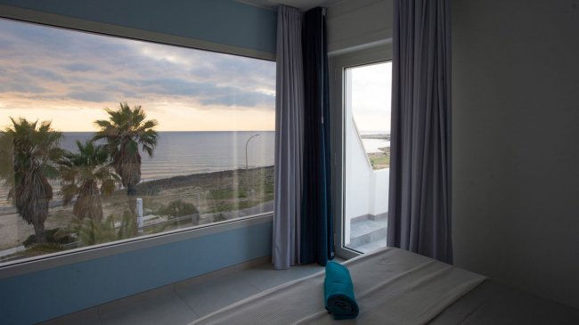 Camera con vista sul mare, palme e tramonto.