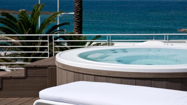 Una vasca idromassaggio su una terrazza con vista sul mare e palme.