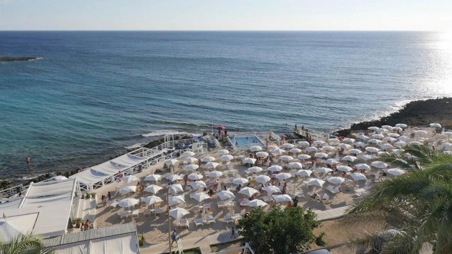Una spiaggia affollata con ombrelloni bianchi vicino a un mare blu.