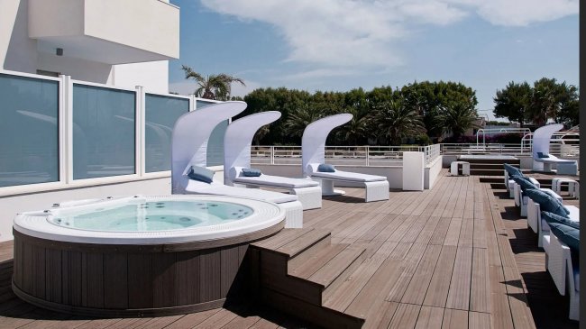 Terrazza con vasca idromassaggio e lettini sotto il cielo azzurro.