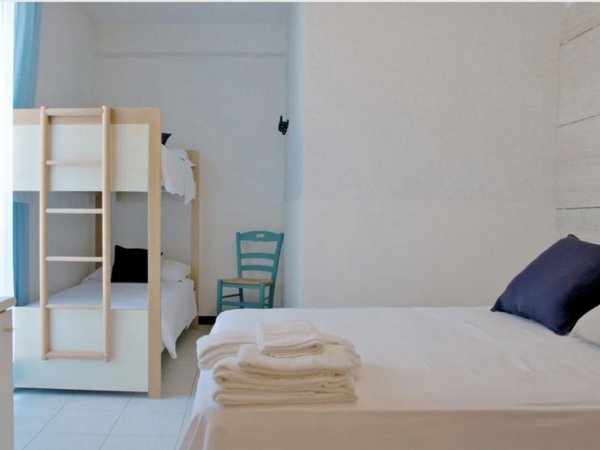 Camera con letto matrimoniale bianco, letti a castello e sedia verde.