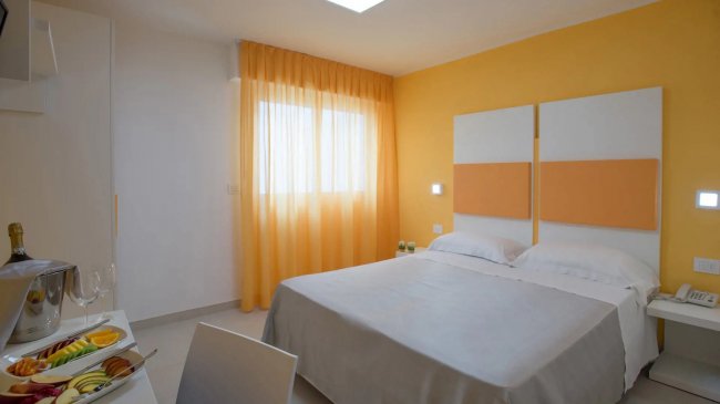 Camera da letto con pareti gialle, letto matrimoniale e tende arancioni.