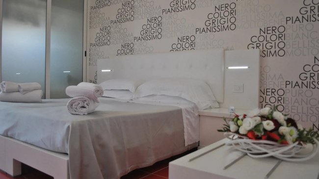 Camera con letto matrimoniale, parete decorata da parole e fiori su un tavolo.