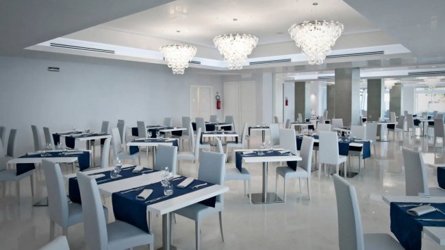 Sala ristorante ampia con sedie grigie, tavoli bianchi e lampadari moderni.