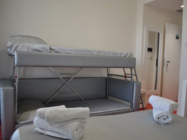 Stanza d'albergo con letto a castello argentato e asciugamani arrotolati.