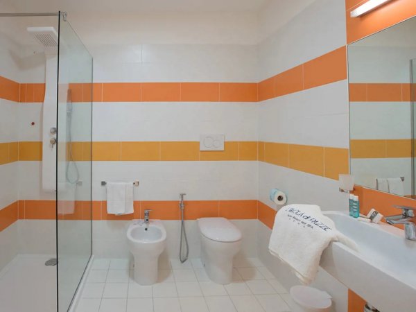 Bagno moderno con doccia in vetro, bidet e wc. Piastrelle bianche con strisce arancioni e gialle.