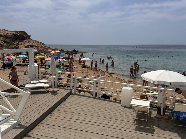 Spiaggia affollata con ombrelloni colorati e persone in acqua; terrazza in legno in primo piano.