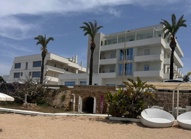 Edificio moderno a più piani con palme e accesso a un tunnel su una spiaggia sabbiosa.