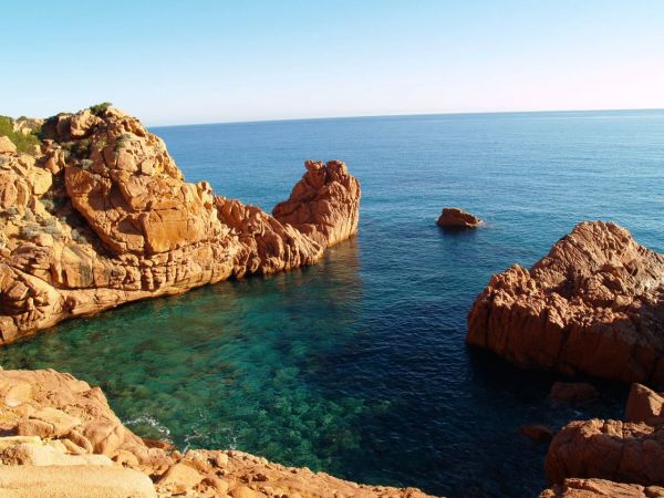 Scogliere rosse circondano acqua cristallina, con rocce emergenti nel mare aperto.
