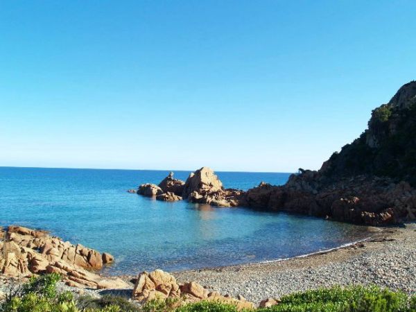 Spiaggia di ciottoli con mare calmo e scogliera.