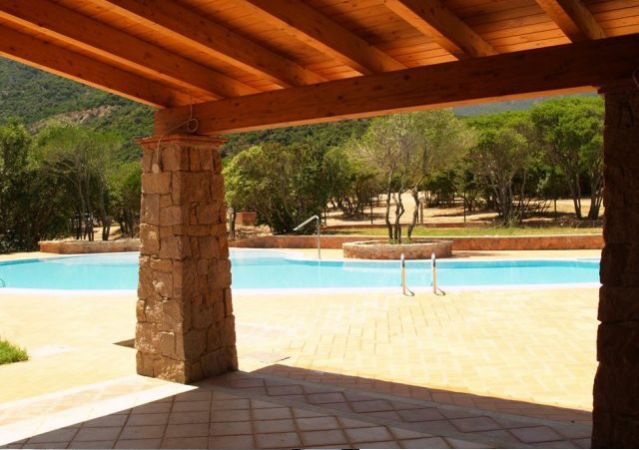 Vista di una piscina da un portico con colonne in pietra e tetto in legno.