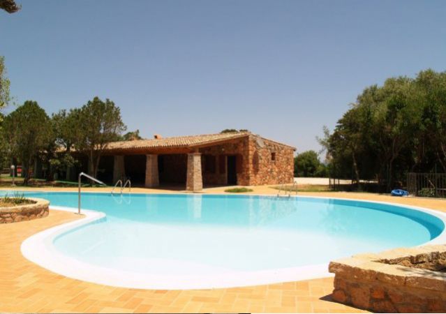 Piscina all'aperto con terrazza in mattoni e casetta in pietra sullo sfondo.