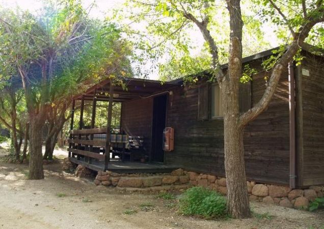 Una casetta in legno in mezzo agli alberi, con una veranda e un tavolo apparecchiato.