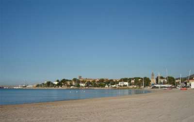 Spiaggia sabbiosa con mare calmo e città sullo sfondo.