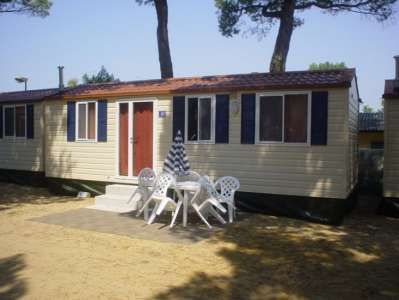 Casa mobile chiara con porte marroni e sedie bianche in un cortile sabbioso.