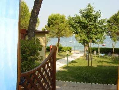 Vista dal cortile con prato, alberi e accesso a un lago.