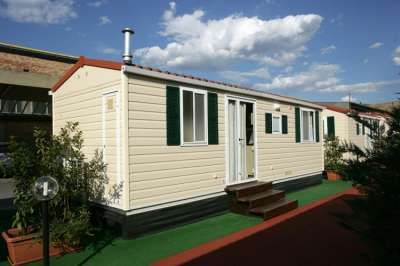 Una casa mobile con pareti bianche e finestre oscurate, situata all'esterno su un prato verde.